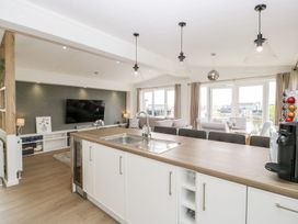 An open plan kitchen and living room with a sink island counter a TV and large windows at Summerdown in Brean