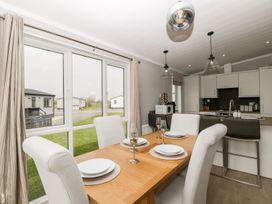 A dining area with a wooden table set for four and a kitchen with white cabinets and bar stools at Summerdown in Brean