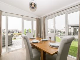 A dining area with a wooden table set with four plates and glasses surrounded by upholstered chairs with large windows overlooking a garden and neighboring houses at Summerdown Brean