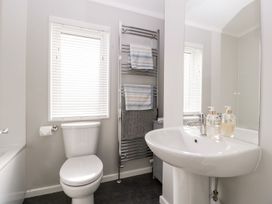 A bathroom with a toilet, sink, towel rack with towels, and a window with blinds at Summerdown Brean