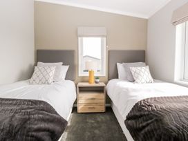 A bedroom with two single beds separated by a wooden nightstand with a lamp and a small plant at Summerdown in Brean
