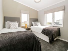 A bedroom with two single beds a nightstand with a lamp and windows at Summerdown in Brean