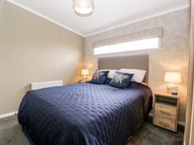 A bedroom with a double bed with blue bedding and bee cushions a nightstand with a lamp and small items at Summerdown Brean
