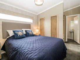 A bedroom with a bed with blue quilt and bee pillows near two wooden wall niches and an open door leading to a bathroom at Summerdown in Brean