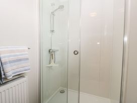 A shower enclosure with a handheld showerhead and glass door next to a towel rack with striped towels at Summerdown in Brean