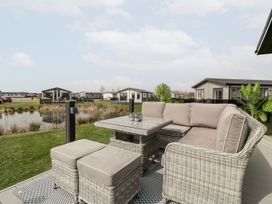 An outdoor seating area with beige cushions and a wicker table on a deck overlooking a pond and modern homes at Summerdown in Brean