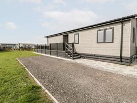 A single-story modular home with a gravel driveway a grass lawn and a black fence at Summerdown Brean