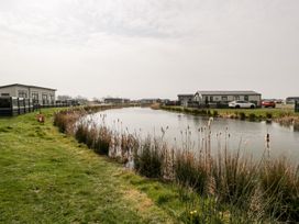 A pond surrounded by grass and reeds with modern homes and cars in the background at Summerdown in Brean