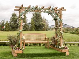 A wooden bench under a floral decorated wooden pergola surrounded by grass at Summerdown in Brean
