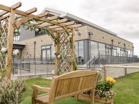 A wooden bench under a pergola with flowers in front of a building with large windows and a ramp at Summerdown in Brean