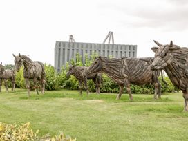 Wooden animal sculptures including cows and horses on grass with bushes and a wooden fence in the background at Summerdown Brean