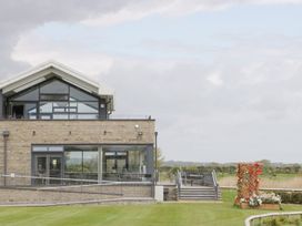 A modern building with glass windows and stone walls with an outdoor seating area and a flower planter on a lawn at Summerdown in Brean