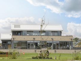 A modern two-story building with large glass windows and a metal roof surrounded by grass and small trees at Summerdown in Brean