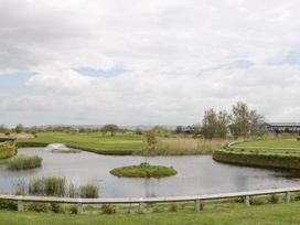 A golf course with a water hazard pond in the foreground and houses in the background at Summerdown in Brean