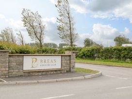 A stone wall with a sign for Brean Country Club with trees and bushes behind it in Brean
