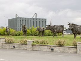 Sculptures of cows and a horse made of wood on a grass lawn behind a low stone wall at Summerdown in Brean