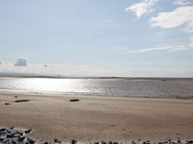 A sandy beach with scattered rocks and patches of grass by the water with clouds in the sky at Summerdown in Brean
