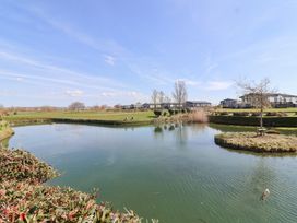 A pond with an island and grass surrounded by houses under a blue sky at Summerdown in Brean