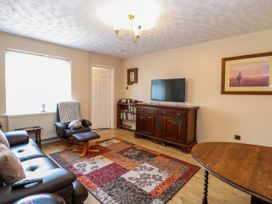 A living room with leather sofa recliner chair wooden cabinet flat screen TV bookshelf and patterned rug at Sweetacres in Hemsby
