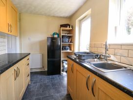 A kitchen with wooden cabinets a black countertop a black refrigerator a sink and a shelving unit at Sweetacres in Hemsby