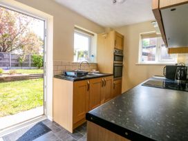 A kitchen with wooden cabinets a sink a stovetop built in ovens a microwave kettle toaster and open door to garden at Sweetacres in Hemsby