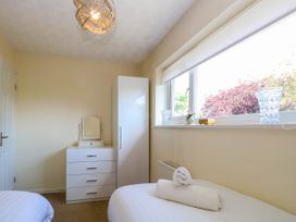 A bedroom with two beds a white chest of drawers a white cabinet and a window with glass items on the sill at Sweetacres in Hemsby