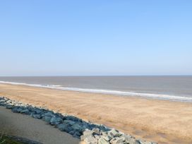 A sandy beach with waves and a rocky barrier along the shore at Sweetacres in Hemsby