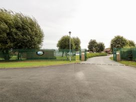 The entrance gate to a green fenced property with a paved driveway and trees inside at Sweetacres in Hemsby
