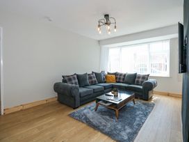 A living room with a gray sectional sofa and checkered cushions a coffee table on a gray rug and a window with blinds at Hendre in Pensarn