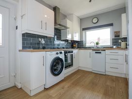 A kitchen with white cabinets wooden countertops a washing machine dishwasher oven and clock on the wall at Hendre in Pensarn