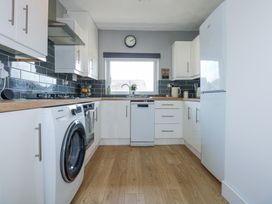 A kitchen with white cabinets a washing machine a refrigerator a sink under a window and wooden floors at Hendre in Pensarn