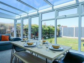 A dining table set with bowls glasses and cutlery next to a sofa with an orange cushion in a conservatory at Hendre in Pensarn
