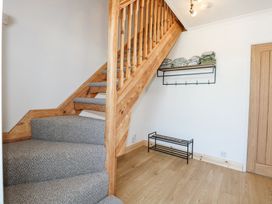A staircase with grey carpet and wooden railing next to a wall with a coat rack and shoe storage at Hendre in Pensarn