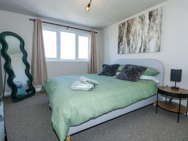 A bedroom with a green bedcover on a bed next to a side table with a lamp and a green standing mirror at Hendre in Pensarn