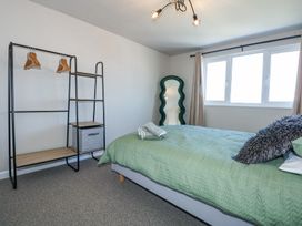 A bedroom with a bed green bedding a clothing rack and a wavy standing mirror at Hendre in Pensarn