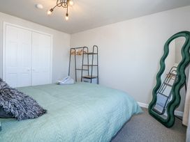A bedroom with a bed covered in a light blue quilt a black and gray pillow a black metal shelving unit with hangers and a green wavy full length mirror at Hendre in Pensarn