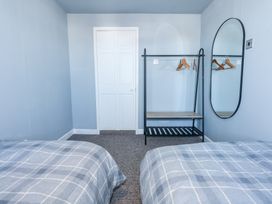 A bedroom with two beds a white door a black clothes rack with hangers and an oval mirror on the wall at Hendre in Pensarn