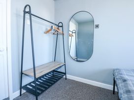 A room with a black metal clothing rack with wooden shelves and hangers a wall-mounted oval mirror and part of a bed with a checkered blanket at Hendre in Pensarn