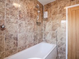 A bathroom with a bathtub shower unit and brown tiled walls at Hendre in Pensarn