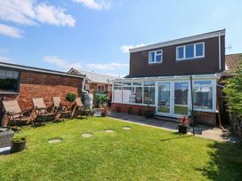 A backyard with lawn chairs along a brick wall and a house with large windows and a patio at Hendre in Pensarn