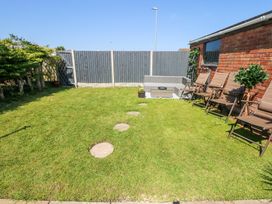 A backyard with green grass a gray fence gray patio sofa brown folding chairs and a brick wall at Hendre in Pensarn
