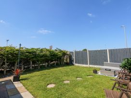 A backyard with a grass lawn surrounded by a hedge and a wooden fence with outdoor seating at Hendre in Pensarn