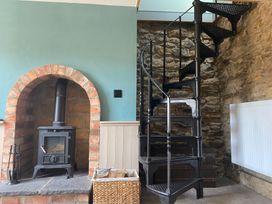 A living room with a wood stove and a spiral staircase at Top Holme Cottage in Newbald