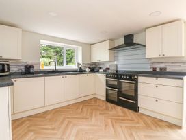 A kitchen with white cabinets black countertops a black stove and a window overlooking green trees at Bewholme in Skipsea