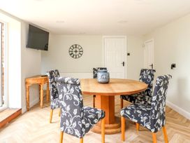 A dining room with a round wooden table six patterned chairs a wall clock and a mounted television at Bewholme in Skipsea