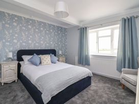 A bedroom with a bed and pillows two nightstands with lamps blue curtains and a window at Bewholme in Skipsea