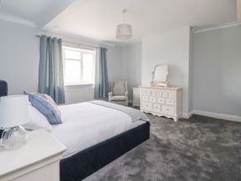 A bedroom with a bed a side table with lamp a grey chair and a dresser with mirror at Bewholme in Skipsea