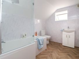 A bathroom with a bathtub shower unit a toilet a white sink cabinet and a small window at Bewholme in Skipsea