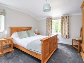 A bedroom with a wooden bed frame two bedside tables lamps a window with curtains and a wooden chair at Bewholme in Skipsea