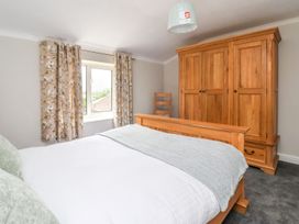 A bedroom with a wooden bed frame white bedding gray throw floral curtains wooden wardrobe and a wooden chair at Bewholme in Skipsea